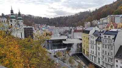 Uprostřed před Vřídelní kolonádou je vidět pára, stoupající ze říčky Teplé.