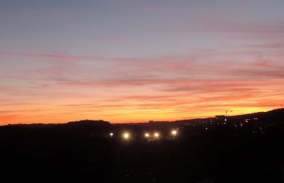 Dnešní západ slunce na sídlištěm Řepy - vpředu září světla na ragbyovém hřišti.