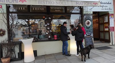Před výlohou Bistra Noll. V oknech odraz domů na protější straně náměstí.